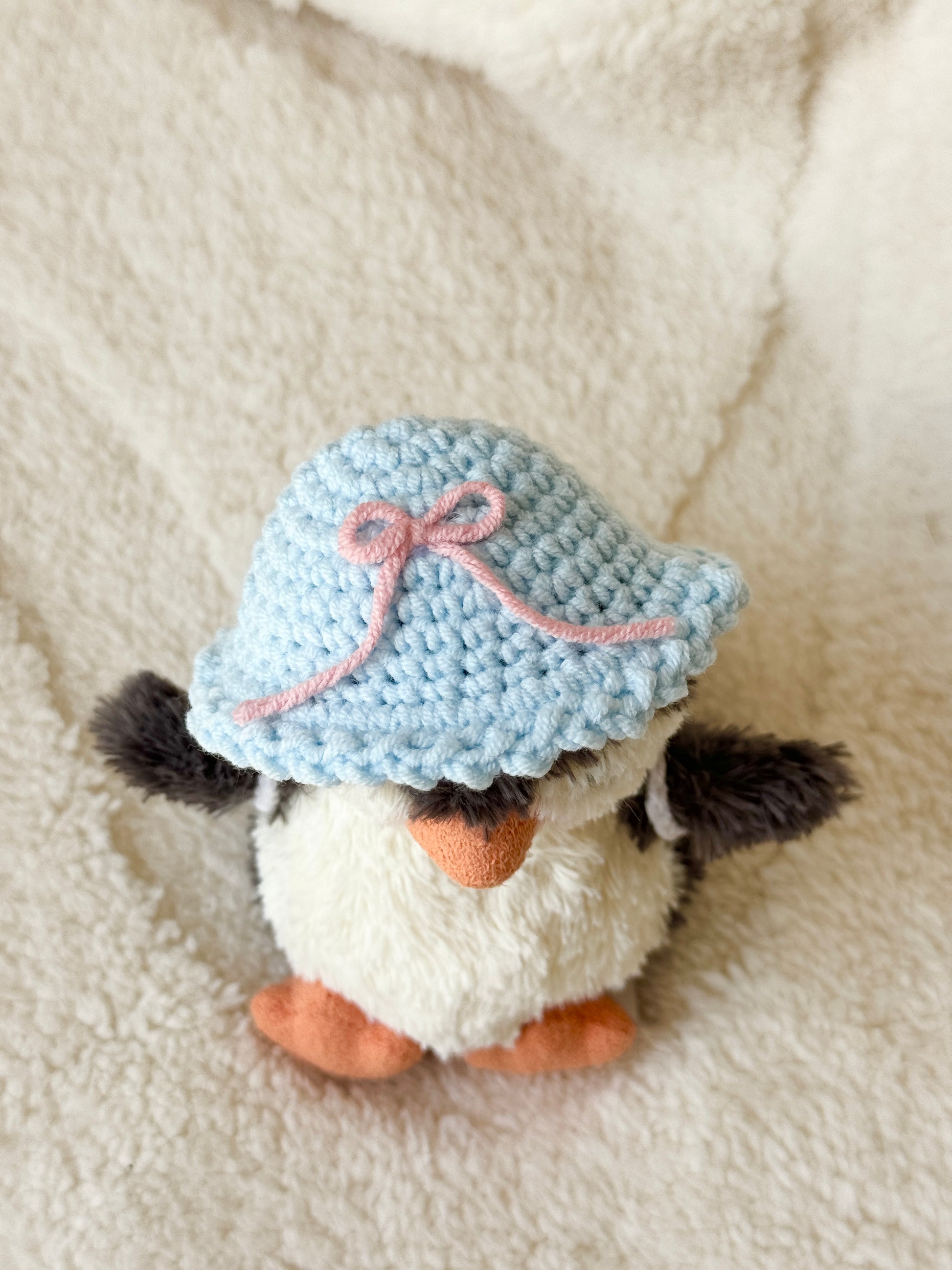 Top-down view of the sky-blue crocheted sun hat with a pink bow on the penguin’s head.