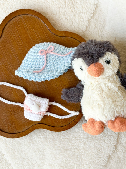 Penguin next to a wooden tray displaying the matching crochet hat and mini backpack set.
