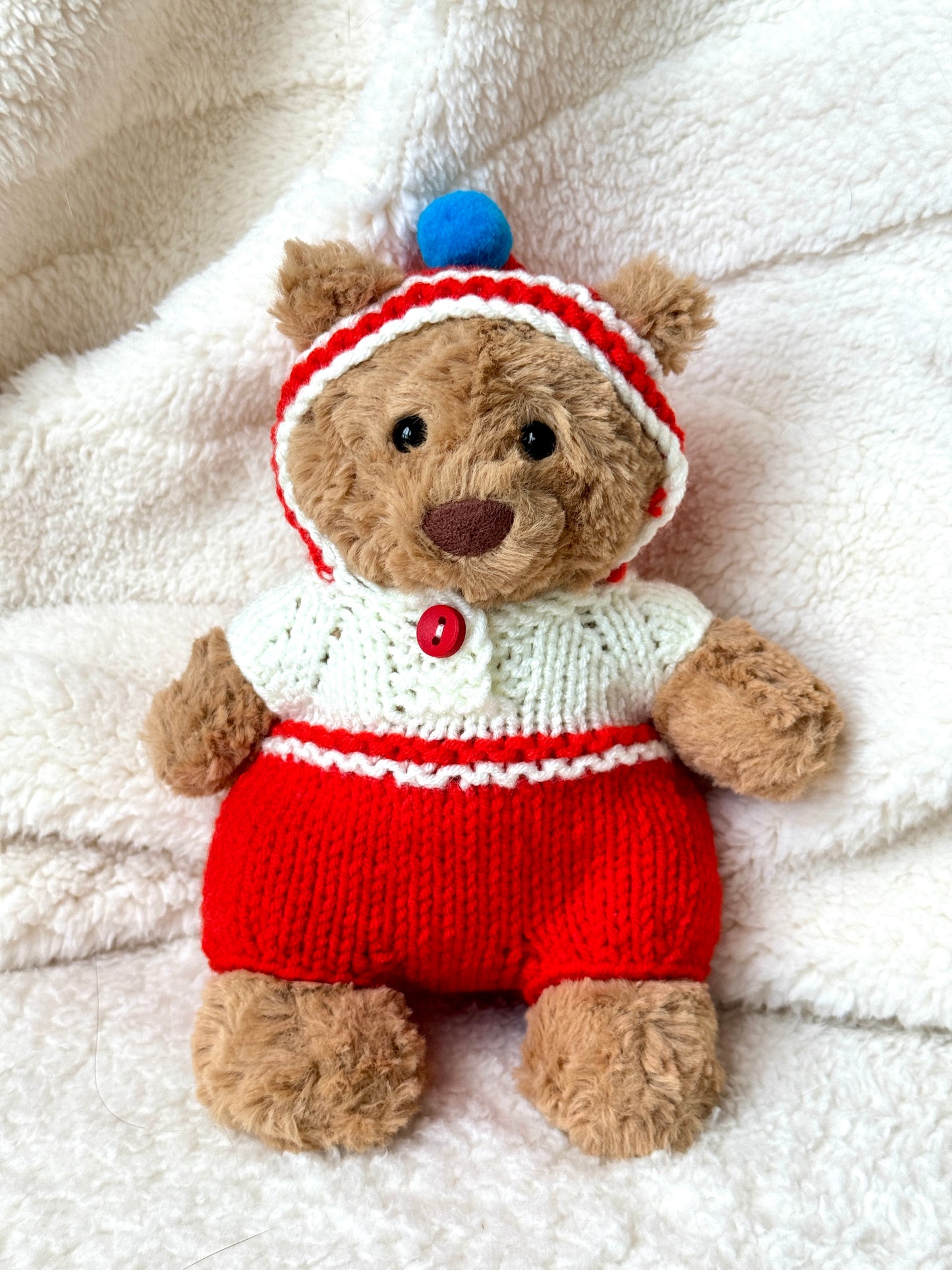 Jellycat Bartholomew Bear wearing red and cream handmade knit onesie with blue pom-pom hood—front view