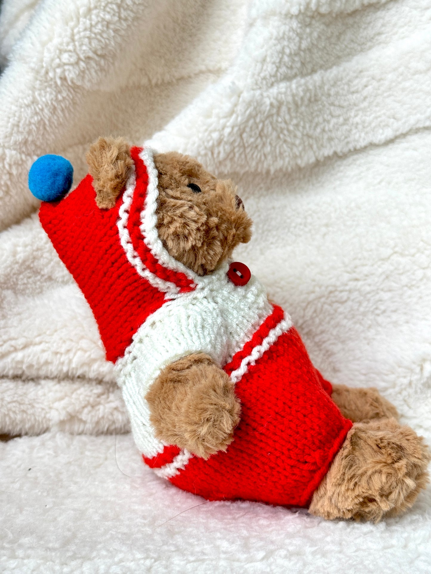 Side profile of Bartholomew Bear in red knit onesie showing snug one-piece fit and hood shape