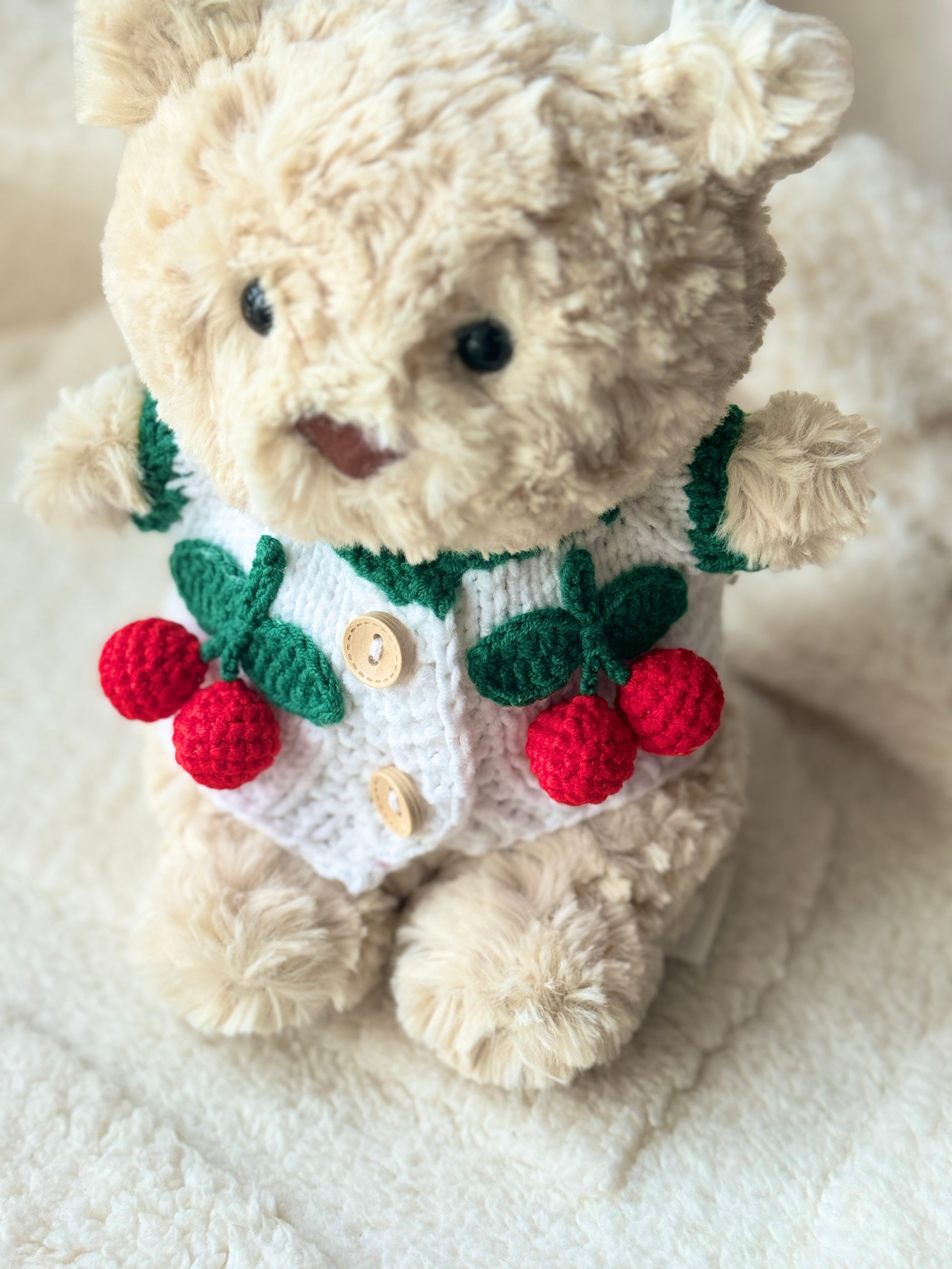Top view of Jellycat Bart Junior in a handmade cherry-themed crochet cardigan, designed as a plush accessory for Bartholomew Bear Junior.