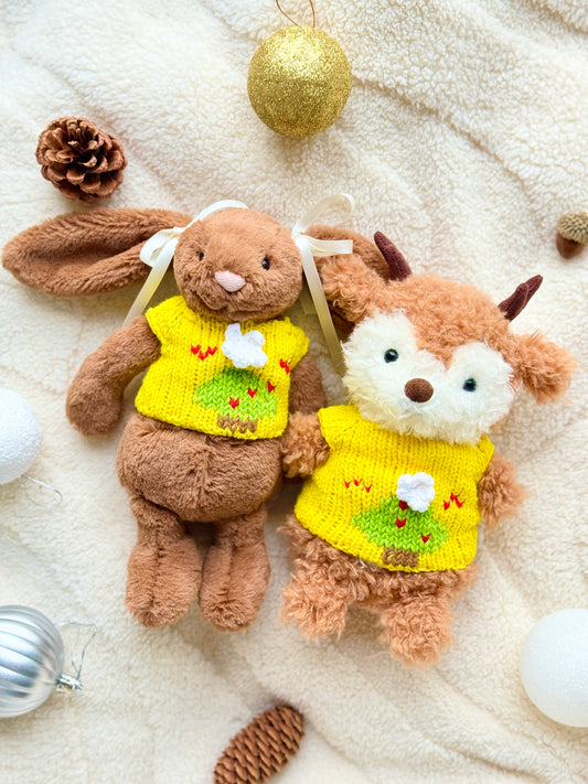 Jellycat Little Bunny and Little Reindeer wearing matching yellow Christmas tree jumpers on a cream blanket with baubles and pinecones.