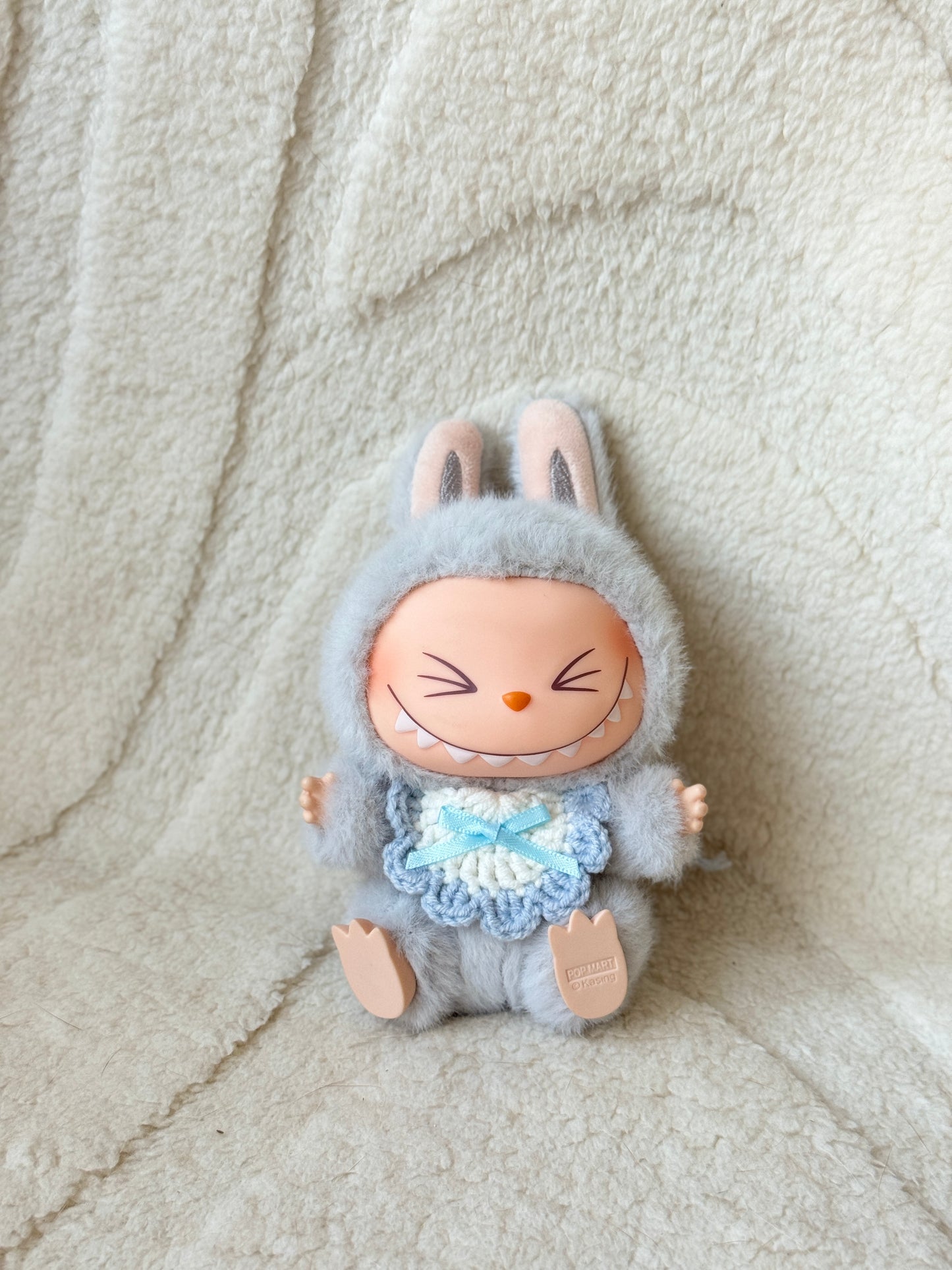 Pop Mart Labubu plush in grey suit wearing a pastel blue crochet bib with lace edges and a satin bow.