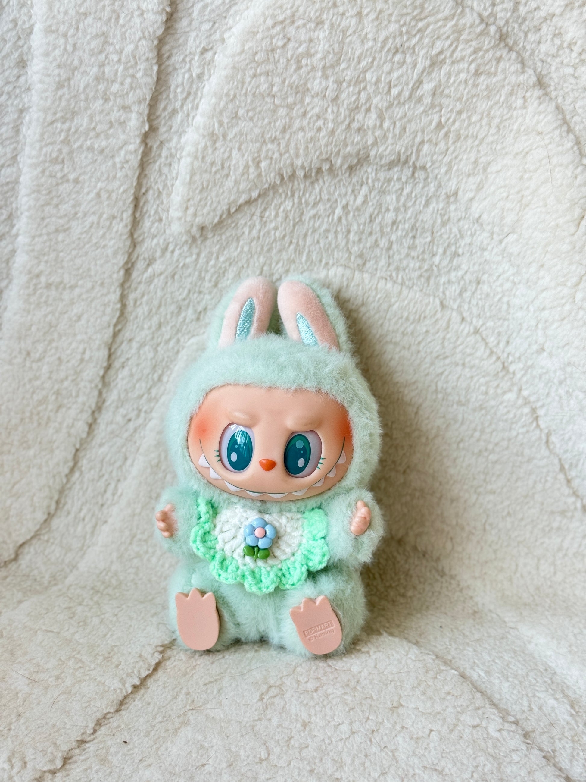 Pop Mart Labubu plush in mint green suit wearing a mint green crochet bib with a small flower in the center.
