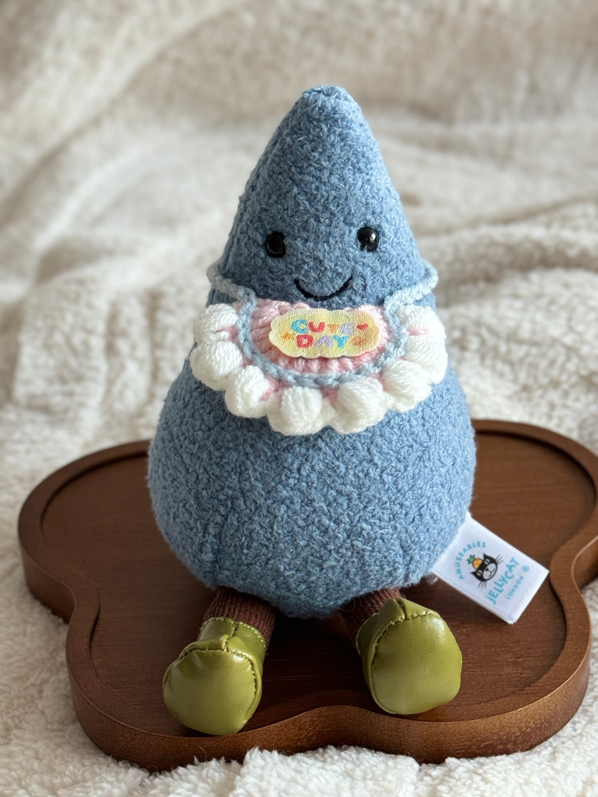 Jellycat Amuseable Raindrop with a pink crochet bib that features a colorful “Cute Day” patch.