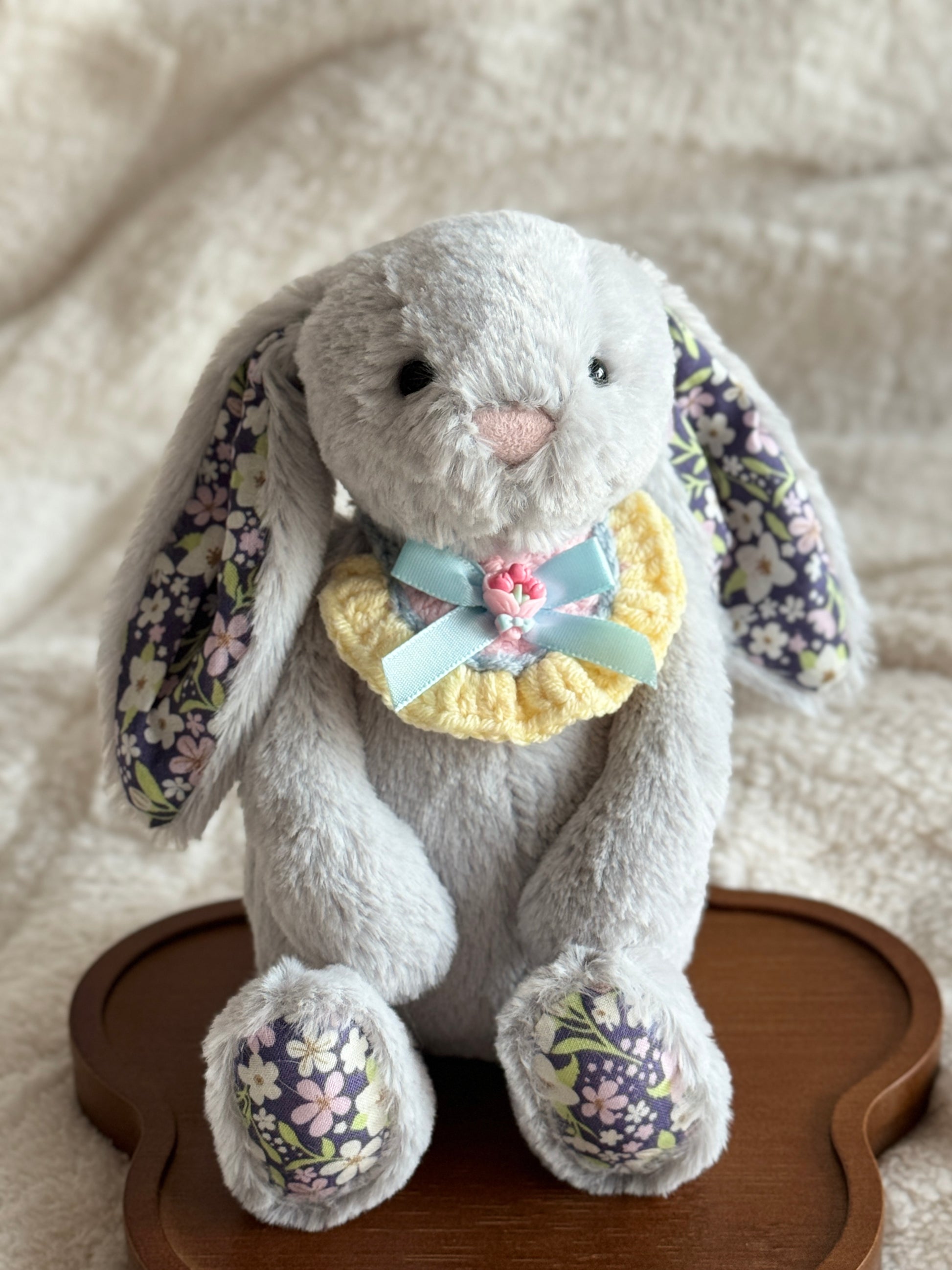 Blossom Bunny Grey wearing a handmade crochet bib with pastel yellow edging, a blue ribbon, and rose embellishment.