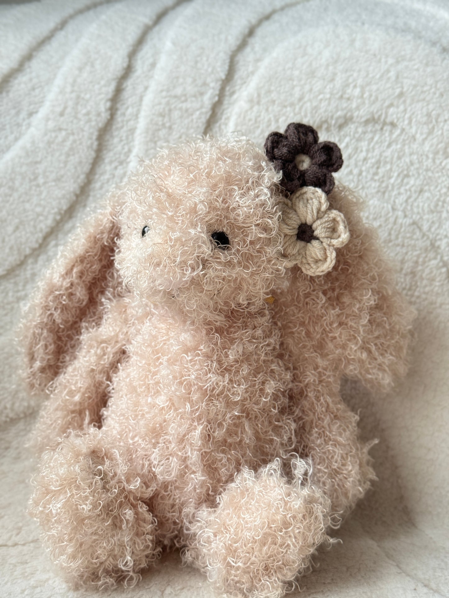 Jellycat bunny plush with curly fur wearing neutral brown and cream handmade crochet flower hair clips on one ear.