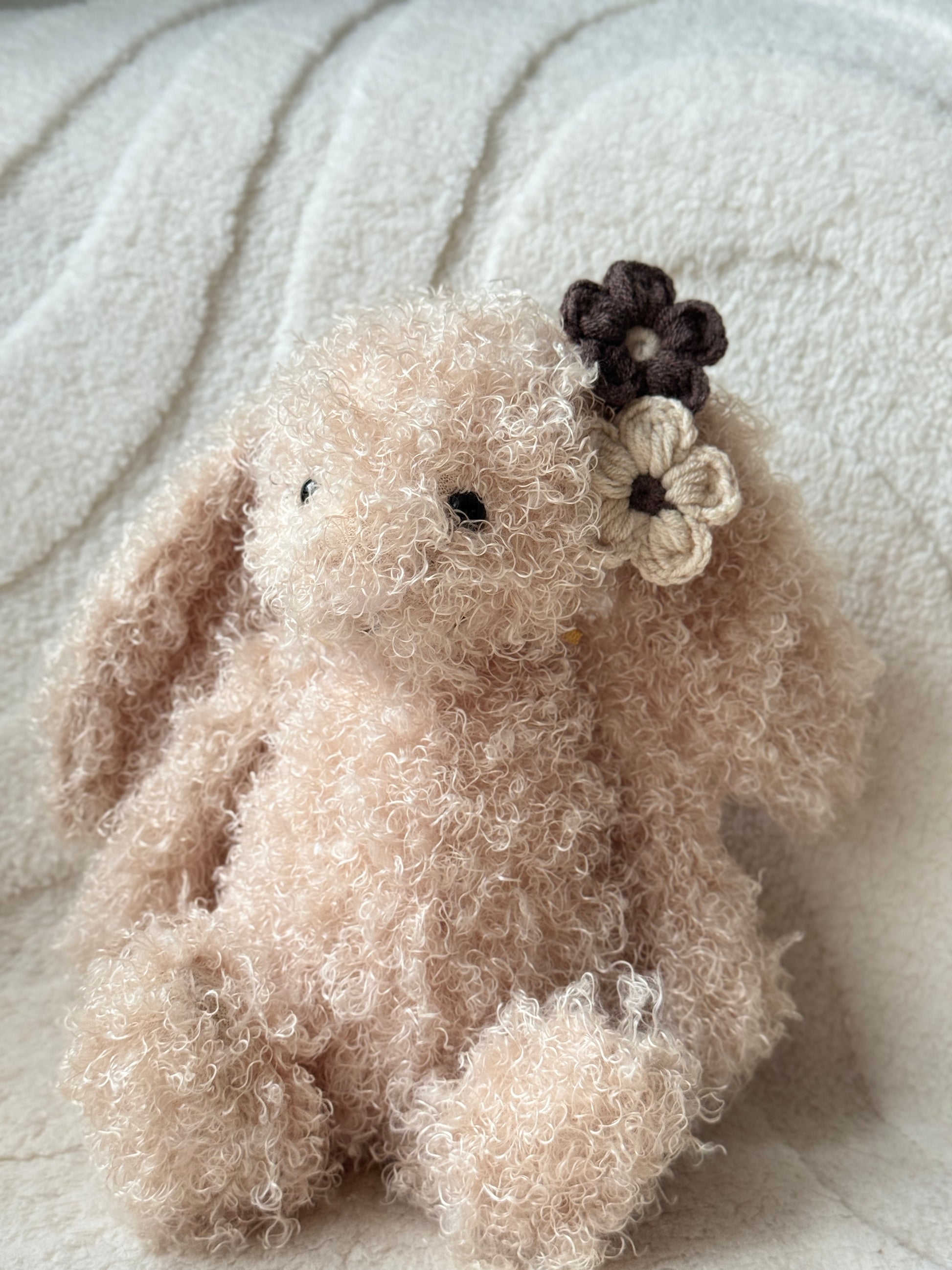Jellycat bunny plush with curly fur wearing neutral brown and cream handmade crochet flower hair clips on one ear.