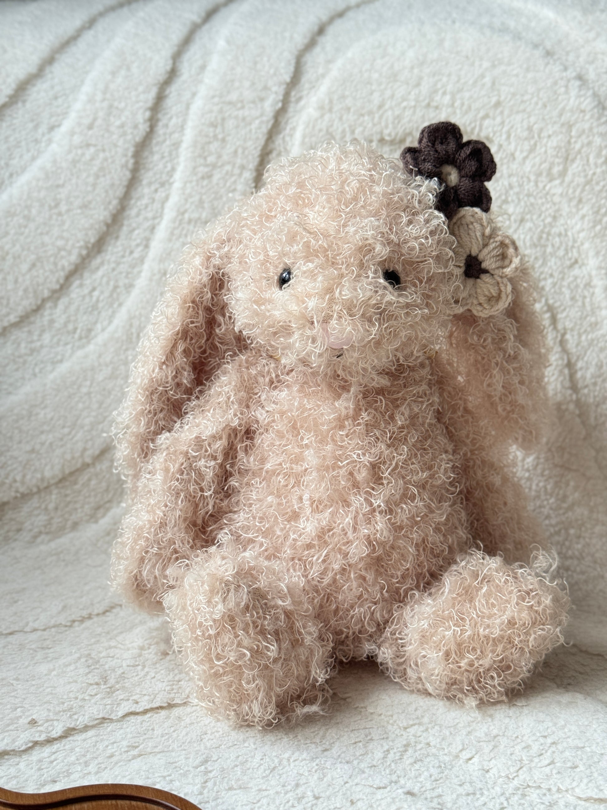 Jellycat bunny plush with curly fur wearing neutral brown and cream handmade crochet flower hair clips on one ear.
