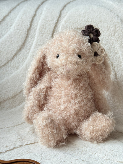 Jellycat bunny plush with curly fur wearing neutral brown and cream handmade crochet flower hair clips on one ear.