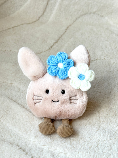 Close-up of a smiling plush toy with blue and white crochet flower hair clips, styled for a cute look.