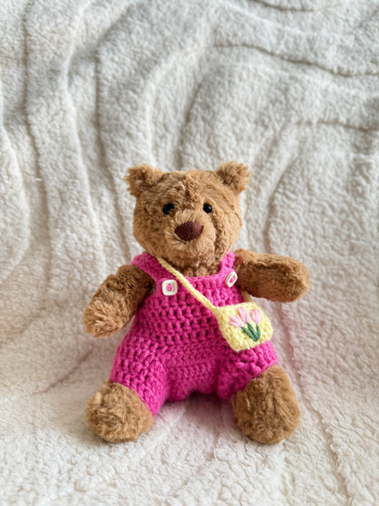 Jellycat Barcelona Bear wearing a bright pink crochet overall with white tulip buttons and a yellow bag embroidered with pink tulips.