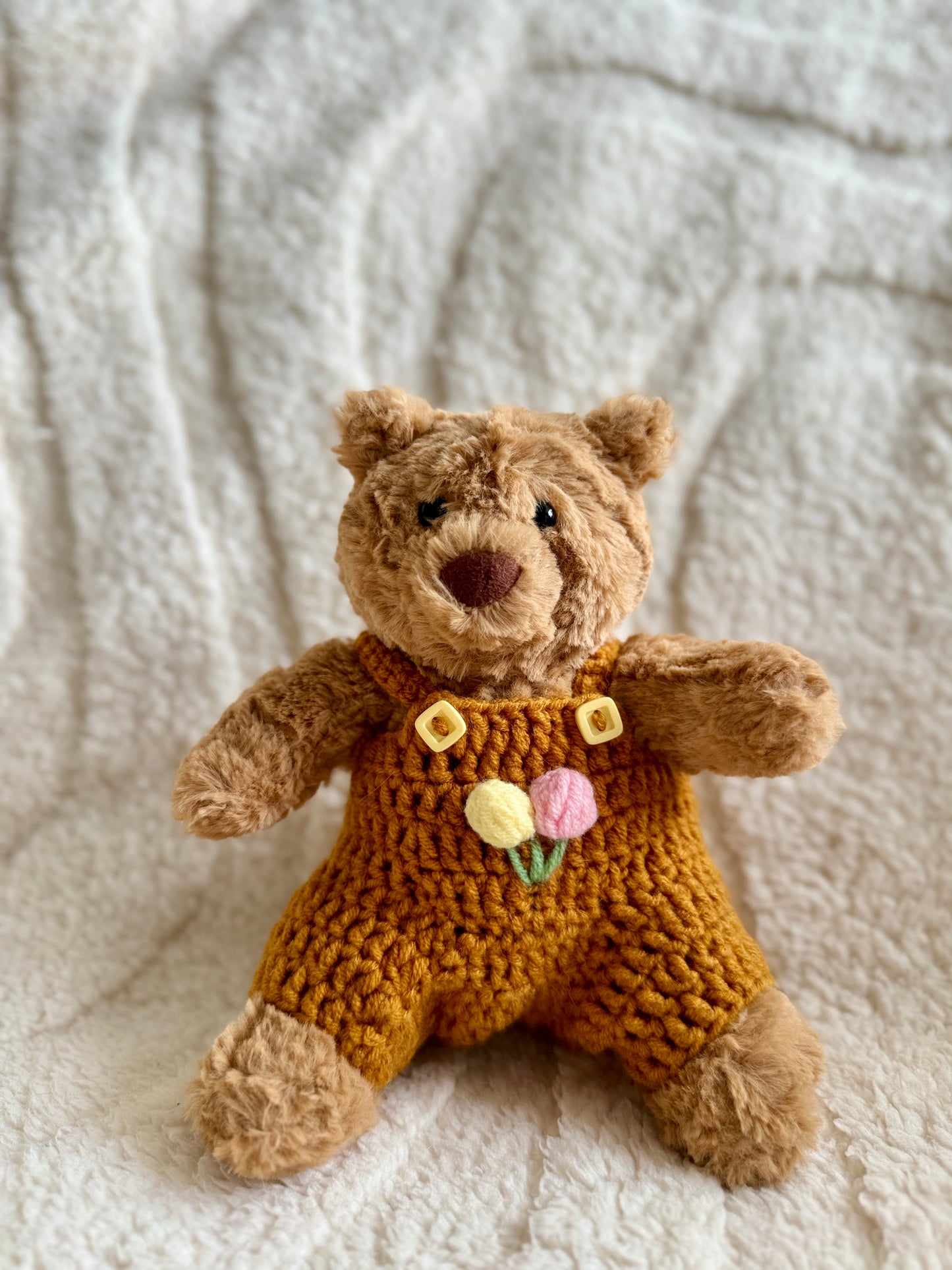 Jellycat Barcelona Bear dressed in a mustard yellow crochet romper with pastel tulip embroidery on the chest.