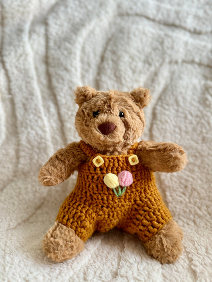Jellycat Barcelona Bear dressed in a mustard yellow crochet romper with pastel tulip embroidery on the chest.
