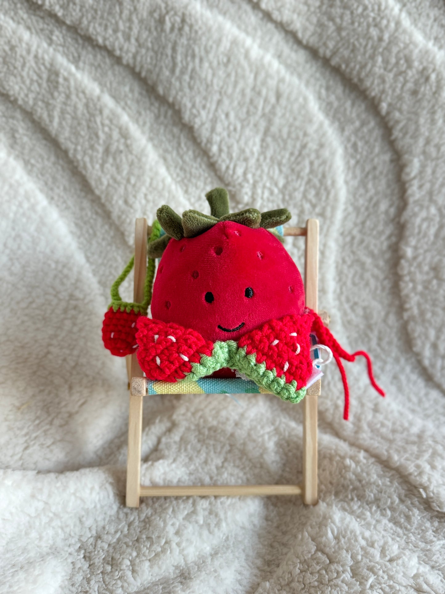 Jellycat strawberry plush wearing a red crochet bikini top with green trim, seated in a mini deck chair.