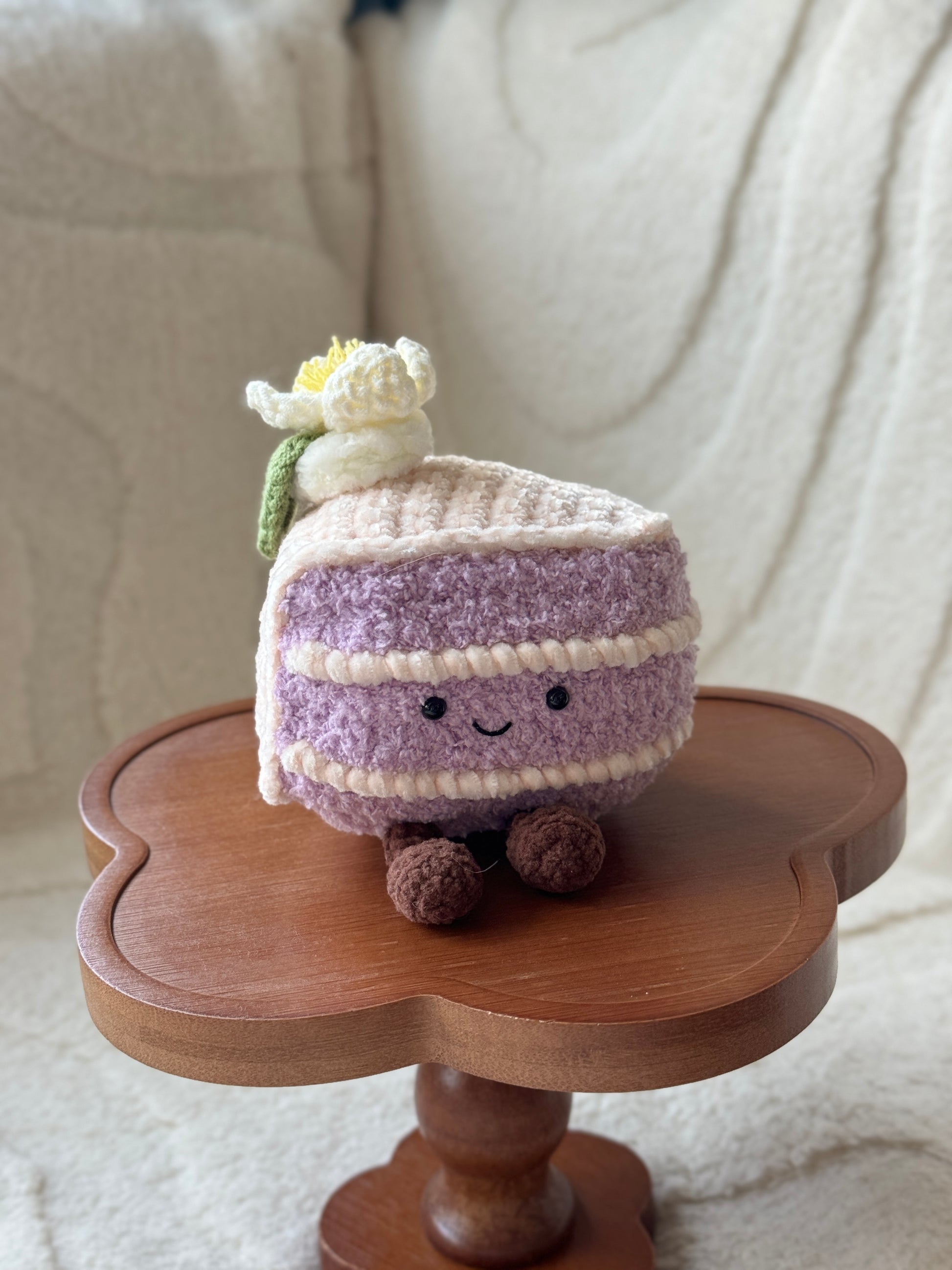 Front view of a crochet taro cake plush with a cute face and brown legs, featuring layered textures and soft pastel tones.