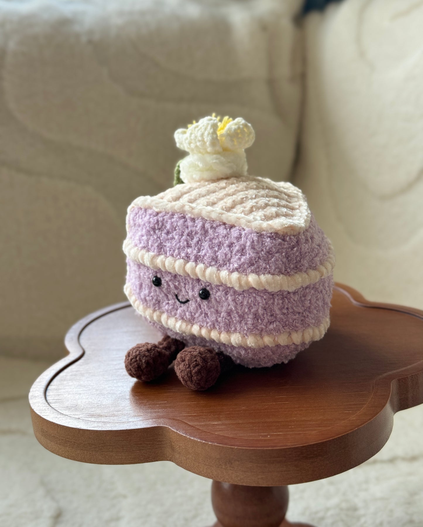 Side view of the handmade taro cake plush showing the cream filling layers and crochet flower on top, displayed on a wooden pedestal.