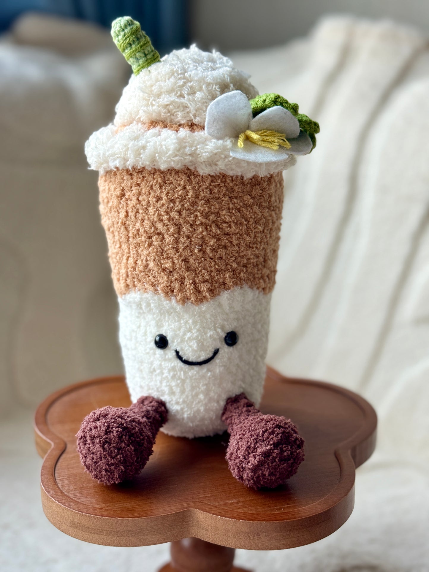 crochet Yulan Latte plush inspired by Jellycat Shanghai edition, with a latte-colored base, fluffy cream top, and white crochet magnolia flower, sitting on a wooden flower-shaped stand.