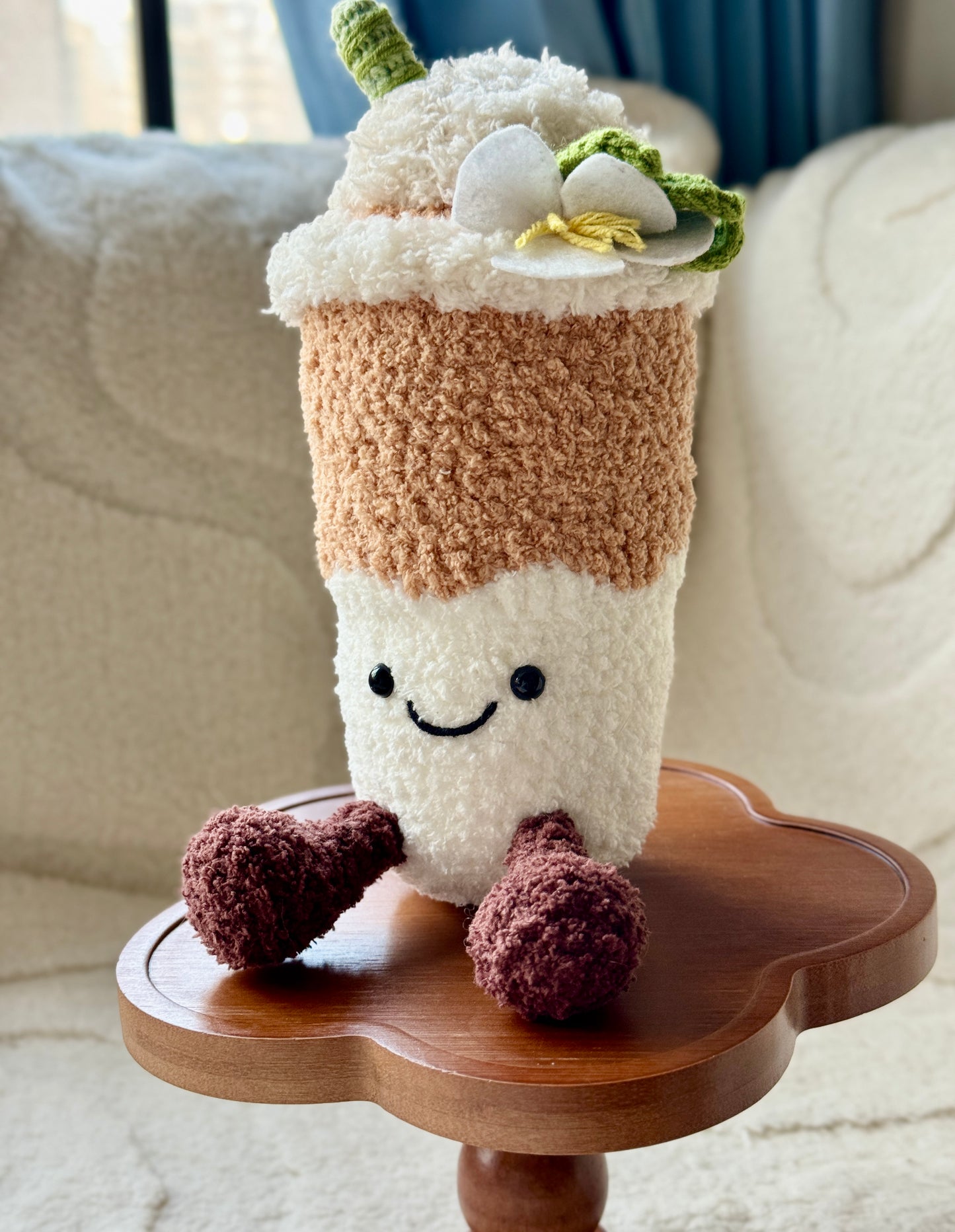 Front view of crochet Yulan Latte plush showing a happy face, brown legs, and white magnolia flower on top, with soft textured yarn.