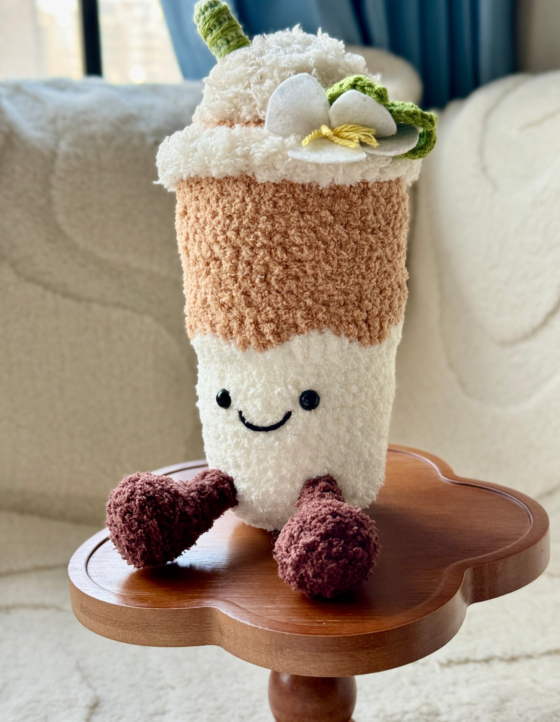 Front view of crochet Yulan Latte plush showing a happy face, brown legs, and white magnolia flower on top, with soft textured yarn.