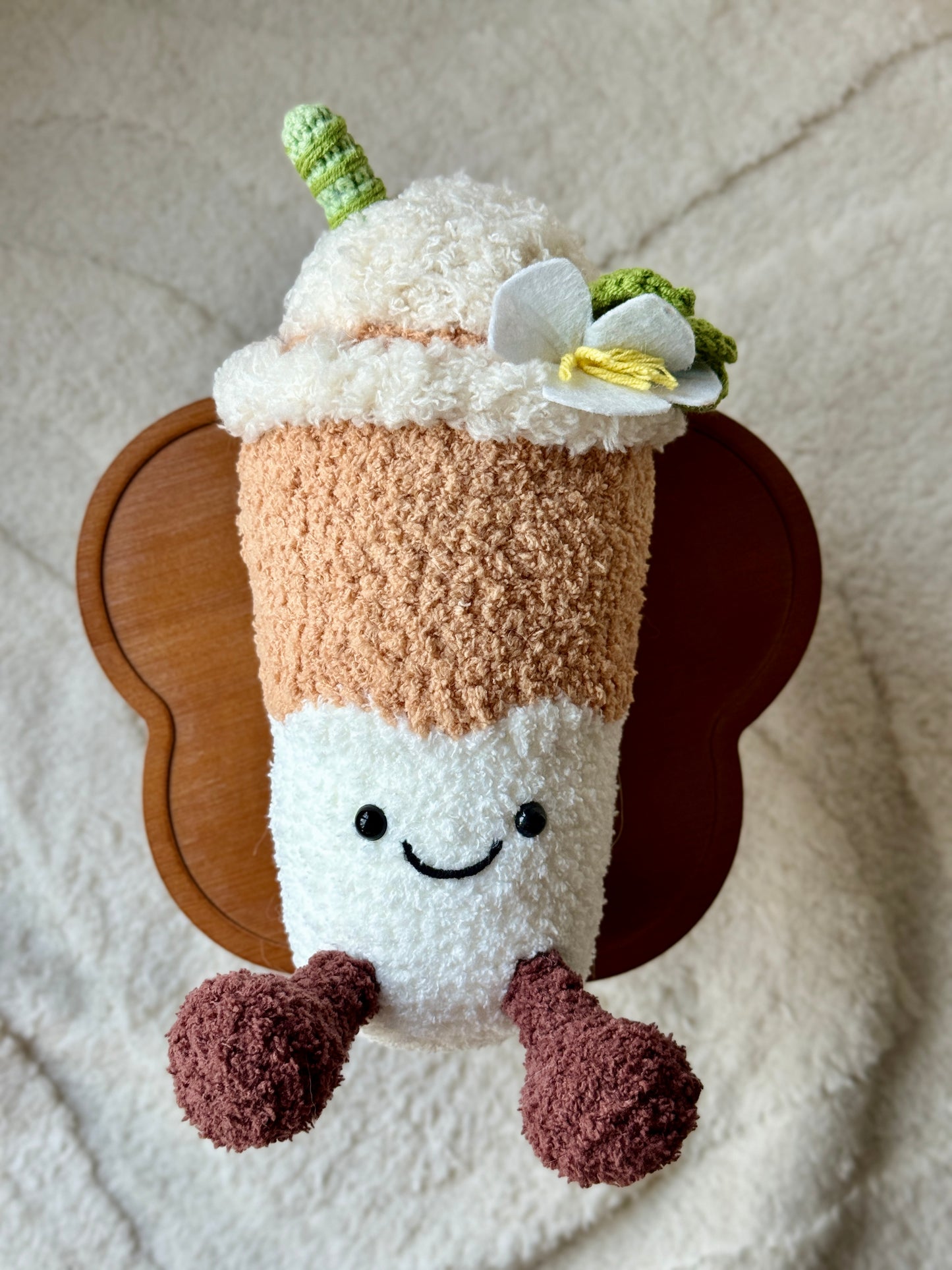 Top-down view of the handmade Yulan Latte plush showing the flower and swirl on top, styled on a wooden cake stand.

