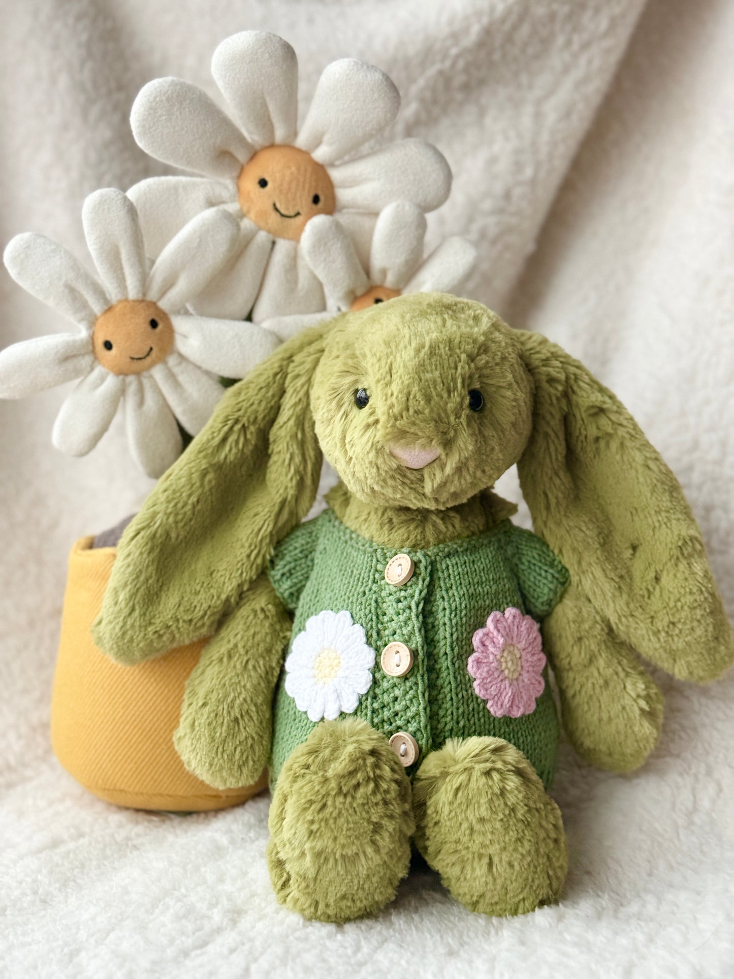 Jellycat Bashful Bunny in sage green daisy cardigan sweater seated beside smiling Jellycat daisy plushies in yellow pot, handmade knit outfit by Z Creations