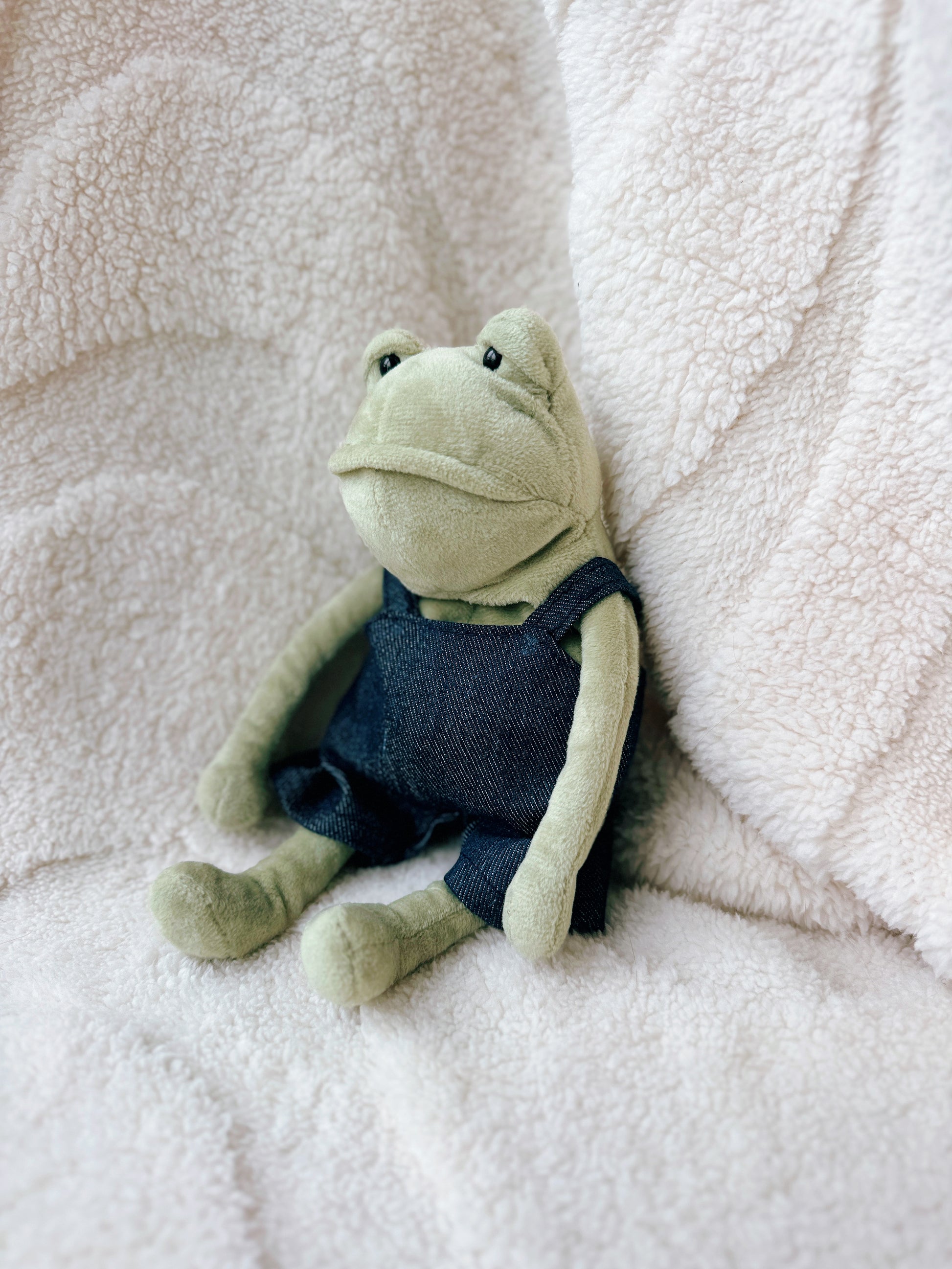 Side view of Jellycat Fergus Frog plush wearing miniature denim overalls