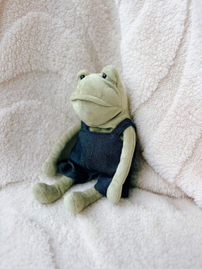 Side view of Jellycat Fergus Frog plush wearing miniature denim overalls
