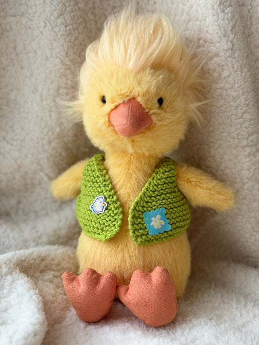 Dorit Duckling wearing a handmade green crochet vest on a soft cream blanket background