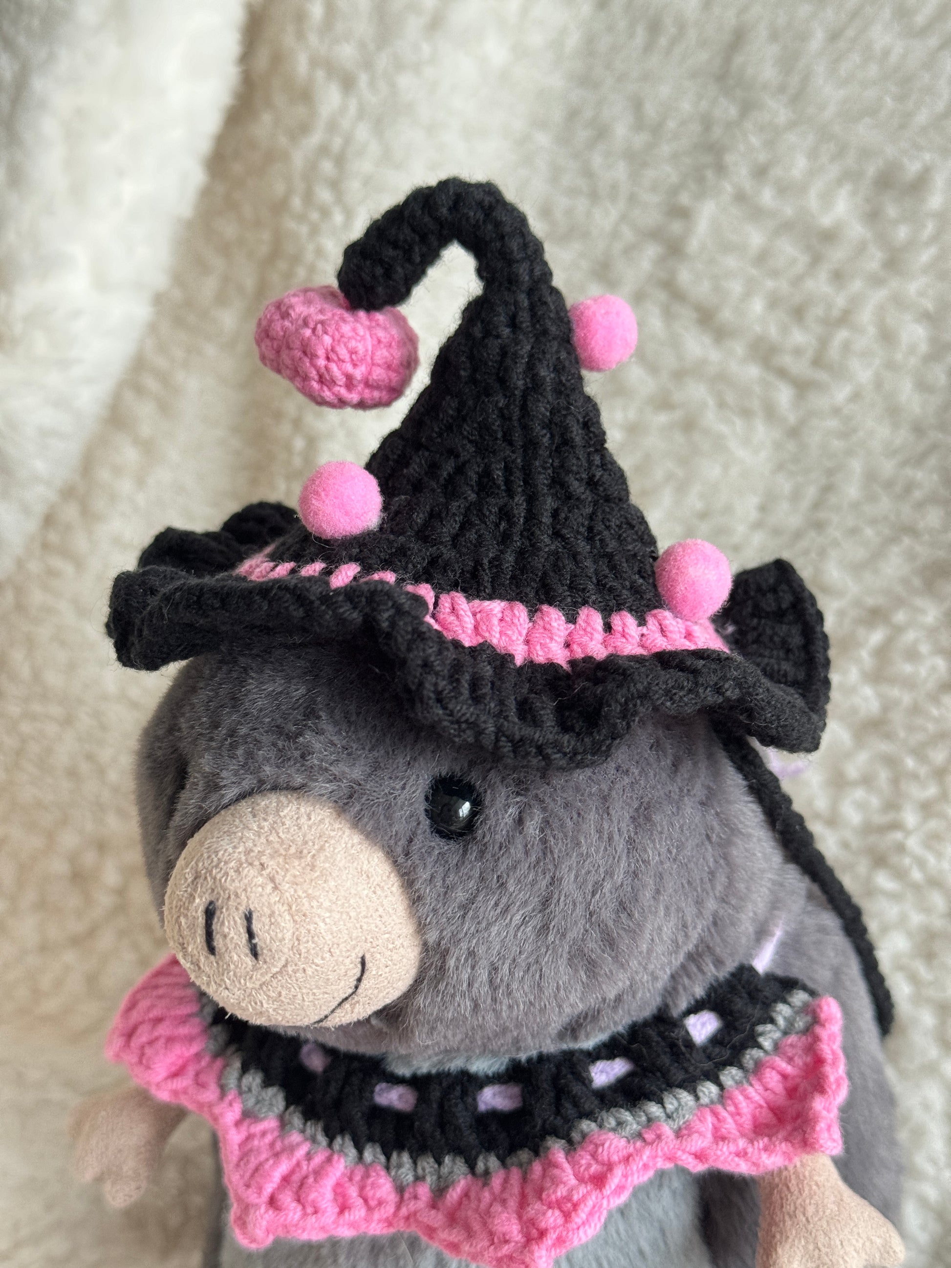Stuffed animal wearing a black and pink crochet hat on a soft surface