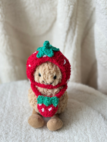 Close-up of Jellycat Peanut in a red strawberry bonnet with green leaf detail and a matching handmade crochet strawberry bag.
