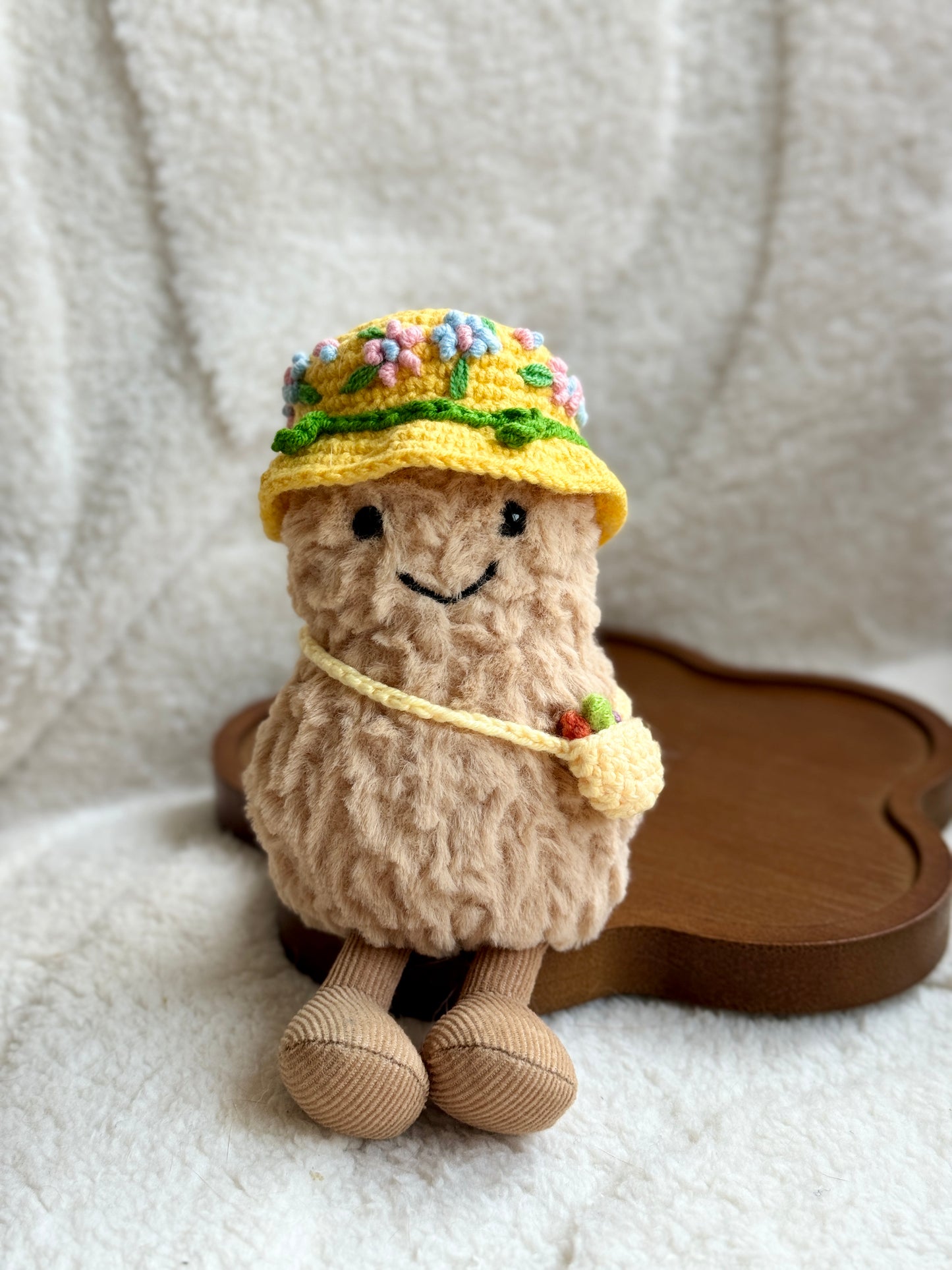 Jellycat Amuseable plush toy wearing a yellow crochet floral bucket hat and crossbody mini bag, sitting on a cream blanket.