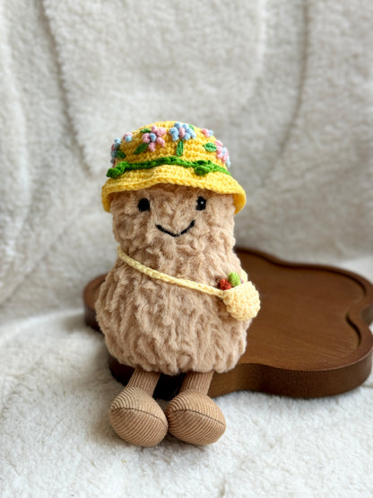 Jellycat Amuseable plush toy wearing a yellow crochet floral bucket hat and crossbody mini bag, sitting on a cream blanket.