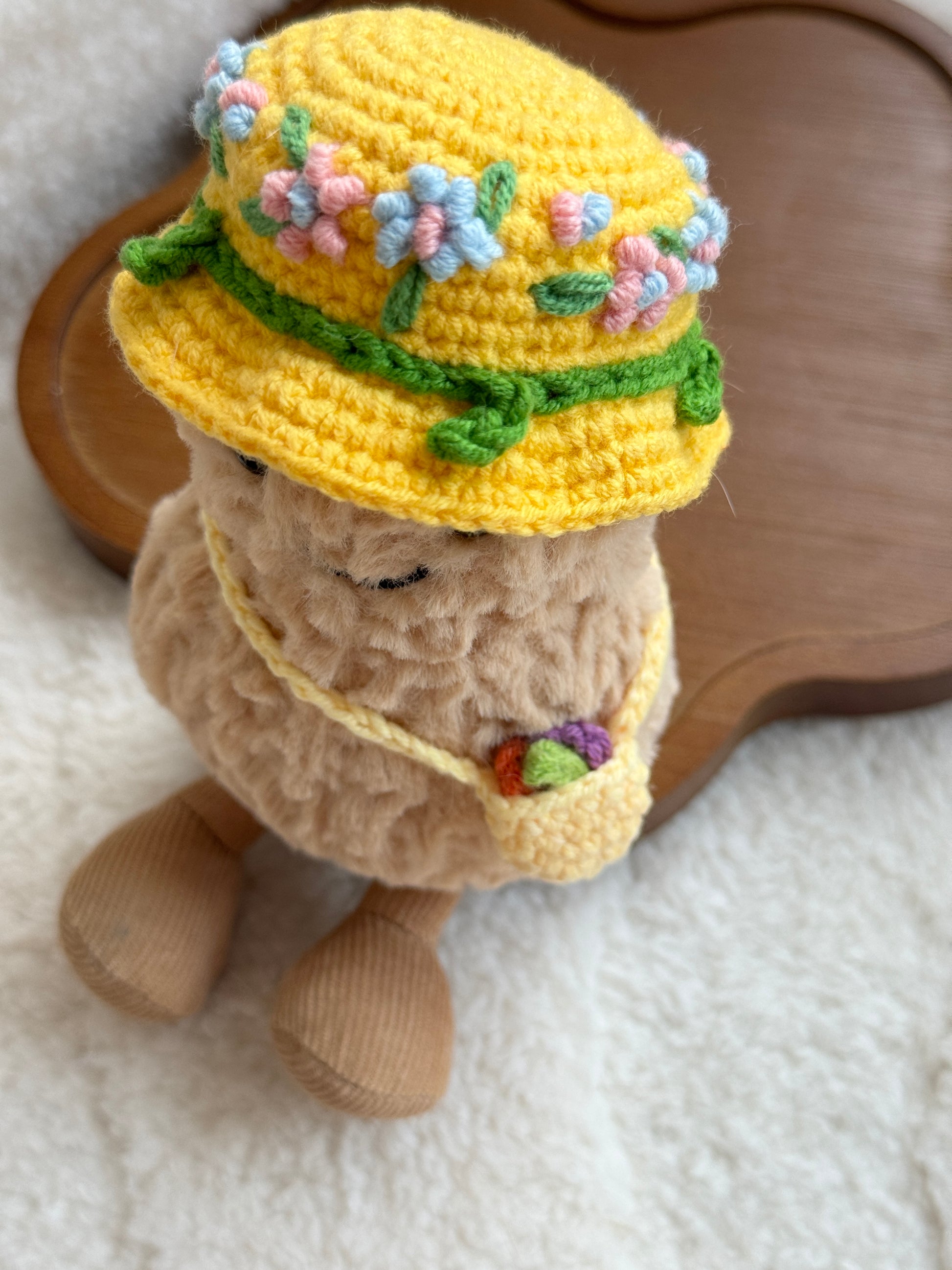 Top-down detail of a crochet hat with pink and blue flowers and a mini yellow bag with small fruit.