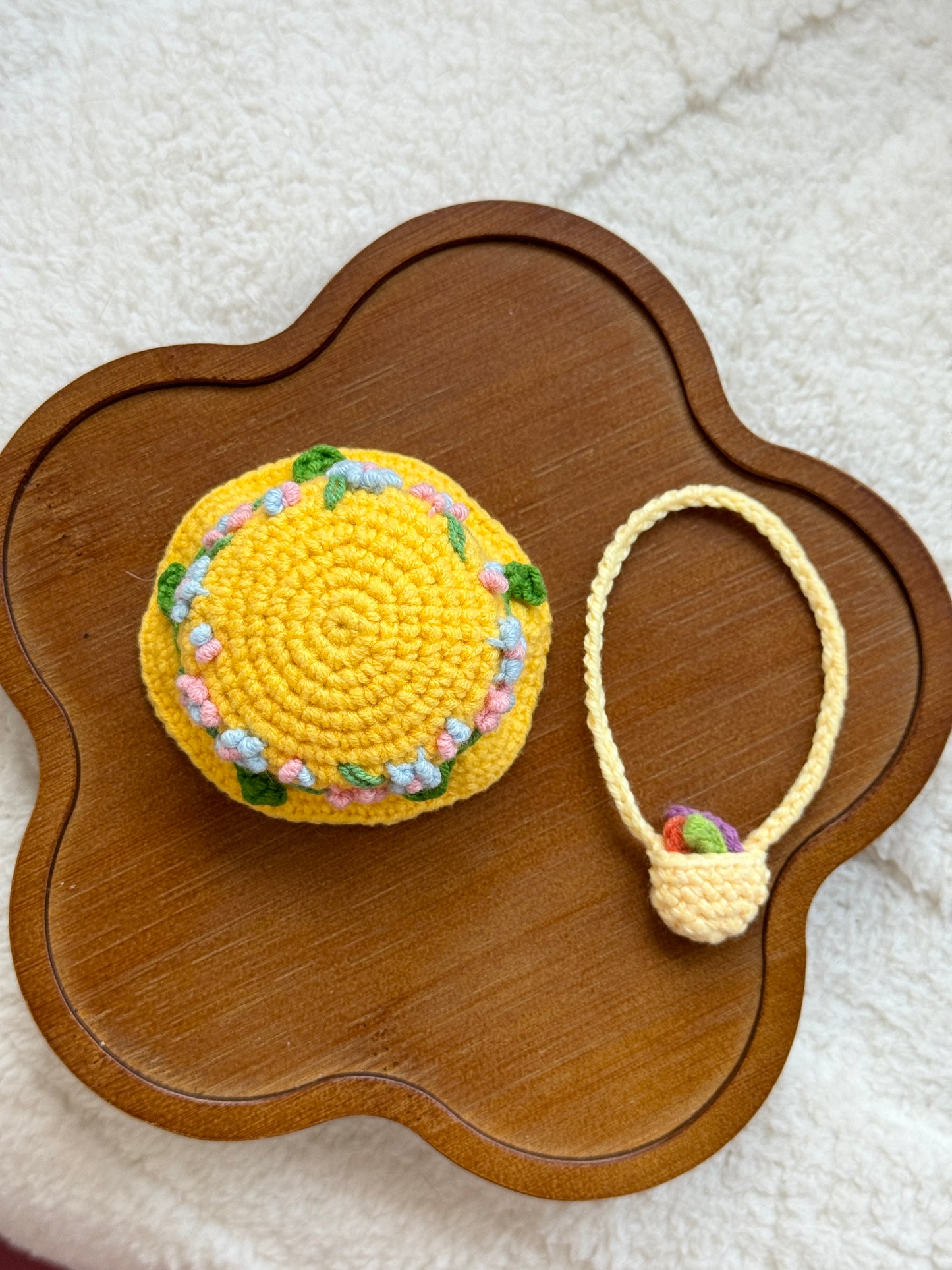 Flat lay of yellow crochet floral hat and mini bag set on a wooden tray.