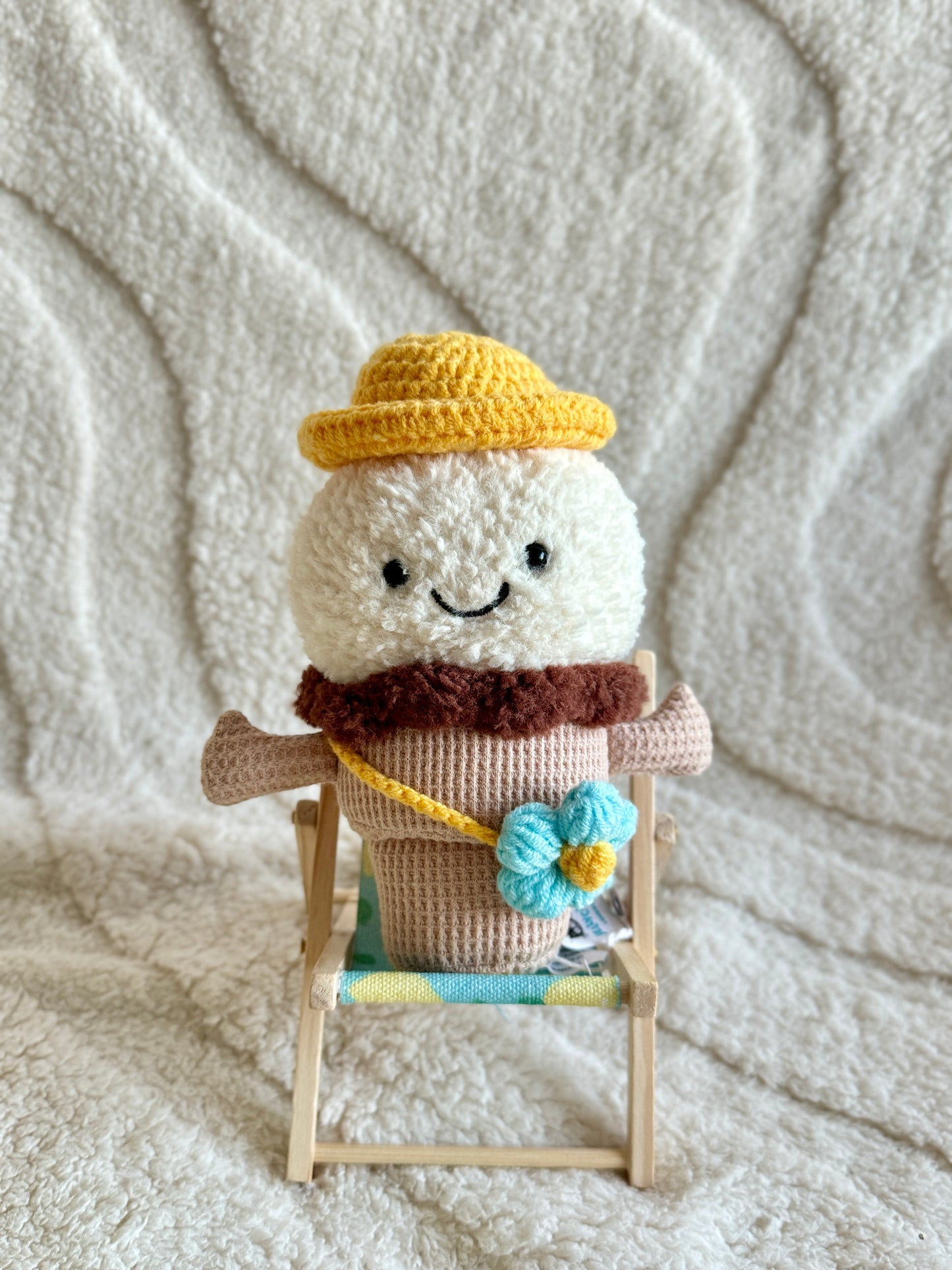 Jellycat Amuseable Ice Cream plush wearing a handmade yellow sun hat and blue flower bag, seated in a miniature deck chair.