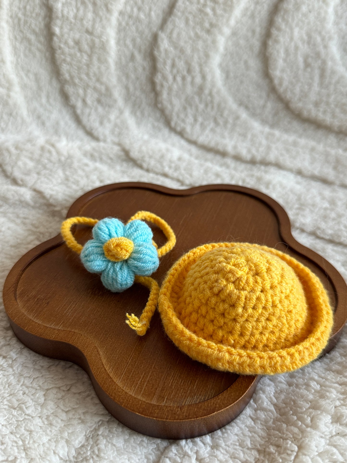 Flat lay of sun hat and flower bag set on wooden tray.