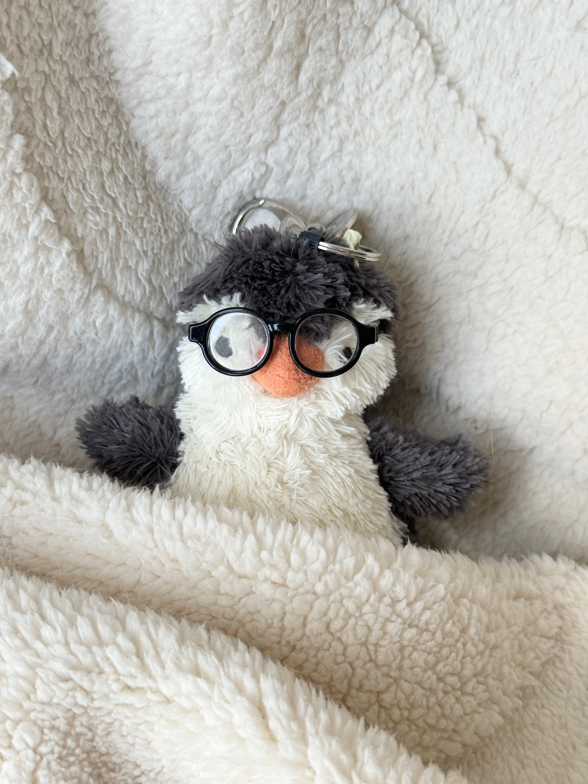 Mini penguin Jellycat bag charm in a cozy blanket wearing tiny black round glasses.