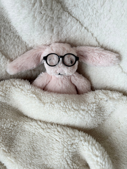 Soft pink bunny Jellycat bag charm resting in a blanket with tiny black round glasses.